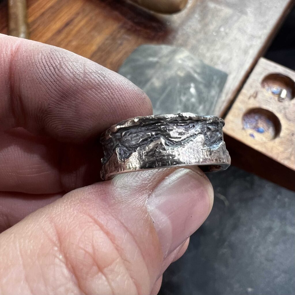 A hand holding a carved Silver ring